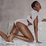 ayra starr strikes a pose in a promo image she is wearing white booty shorts a white top with an opening at the back and knee