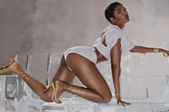 ayra starr strikes a pose in a promo image she is wearing white booty shorts a white top with an opening at the back and knee