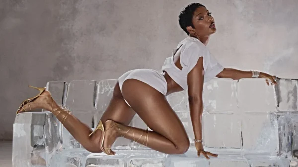 ayra starr strikes a pose in a promo image she is wearing white booty shorts a white top with an opening at the back and knee